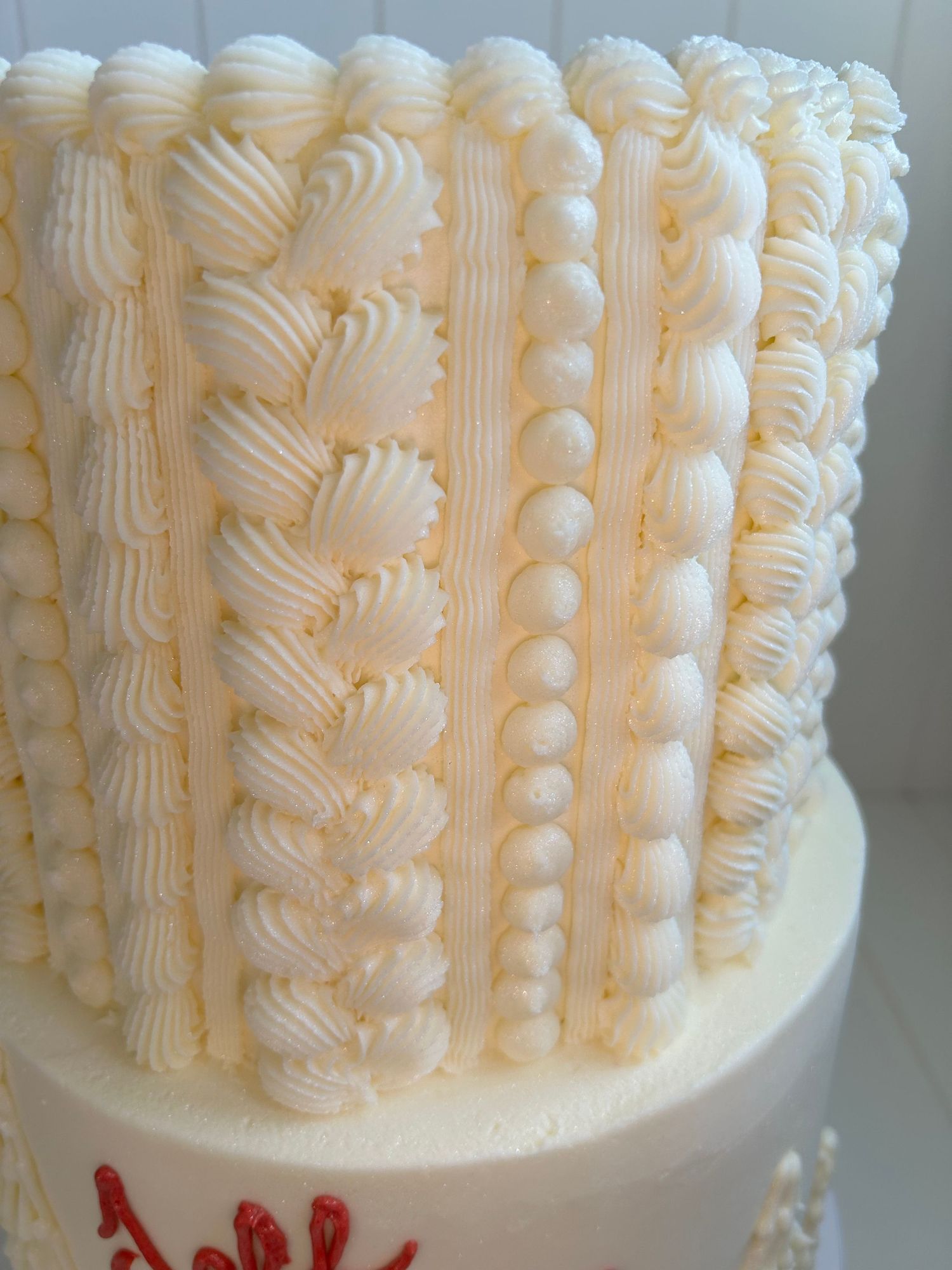 White buttercream cake with intricate vertical piped details creating a textured pattern.