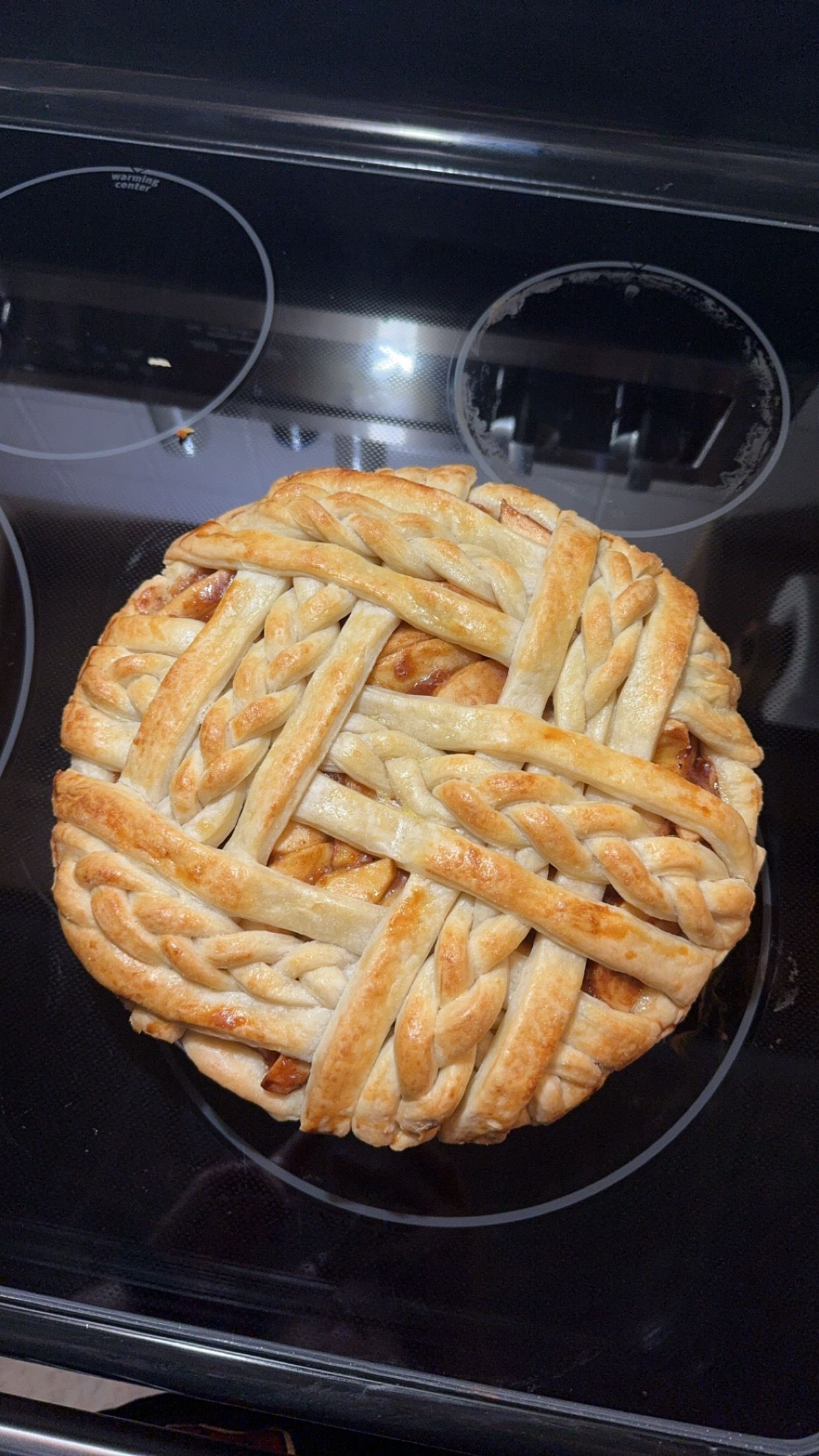 Golden brown lattice apple pie fresh from the oven on a black stovetop.