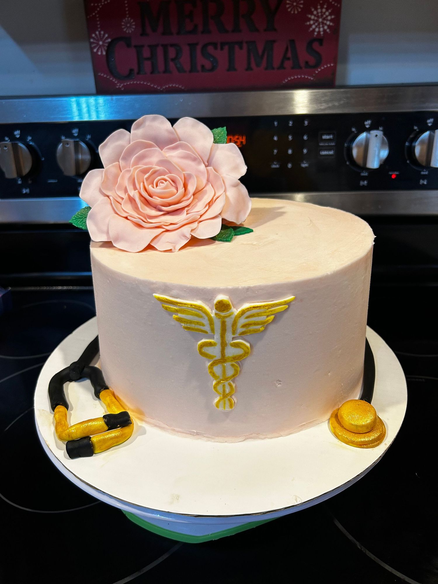 A white medical-themed cake with a caduceus symbol and pink rose decoration.
