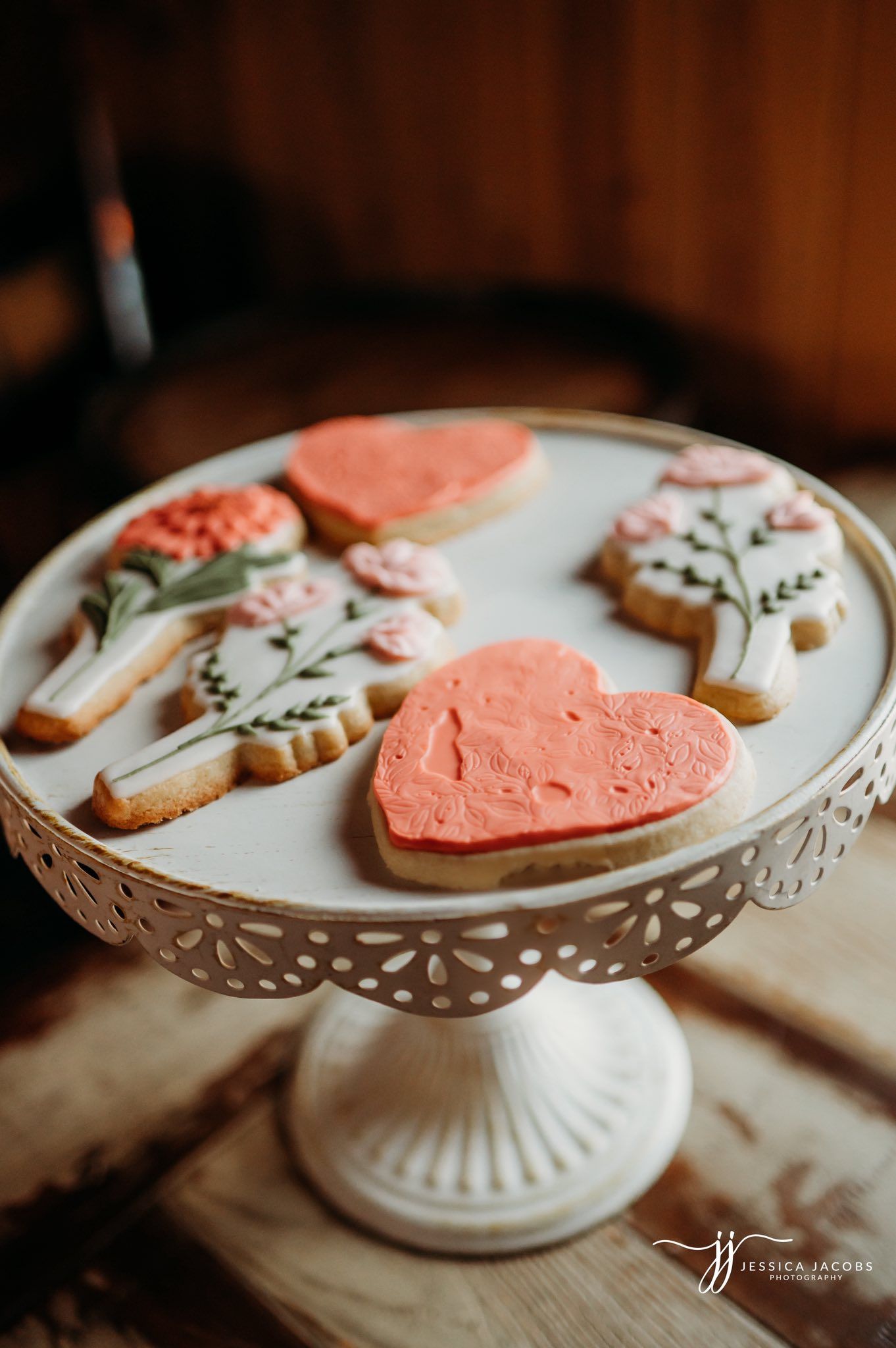 Heart-shaped cookies with coral frosting displayed on white pedestal cake stand.