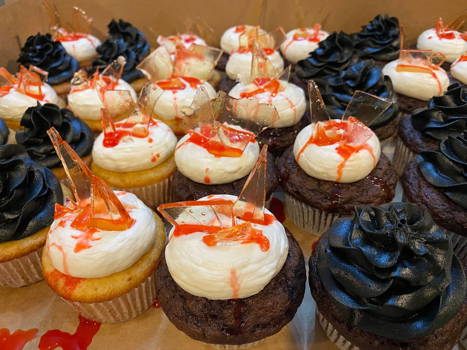 Chocolate and vanilla cupcakes topped with red-tinted frosting drizzle arranged in neat rows.