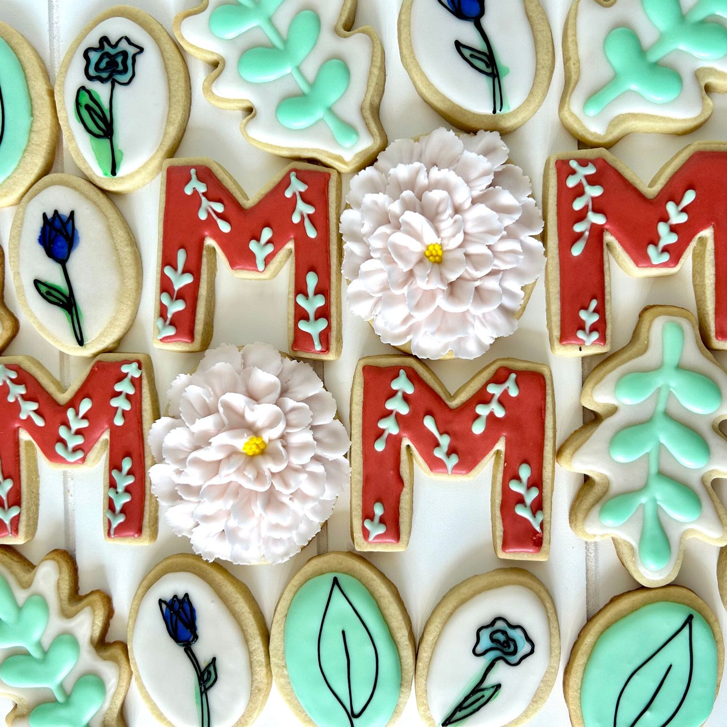 Floral sugar cookies decorated with mint green and red designs featuring leaves and flowers.
