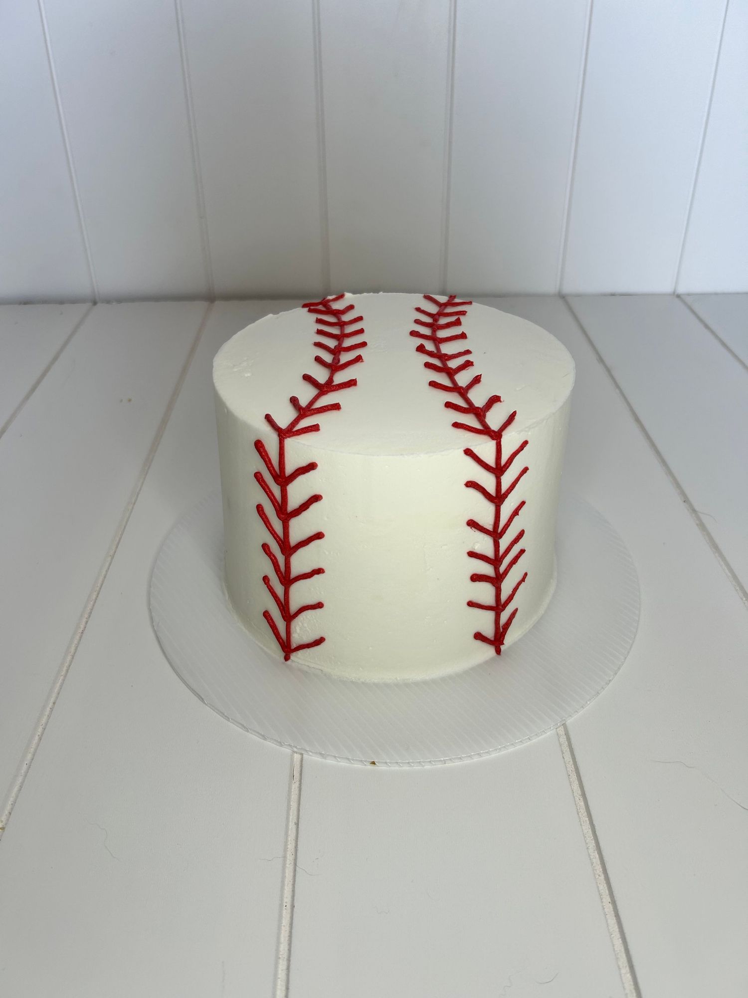 Baseball-themed cake with red stitching pattern on white buttercream frosting.