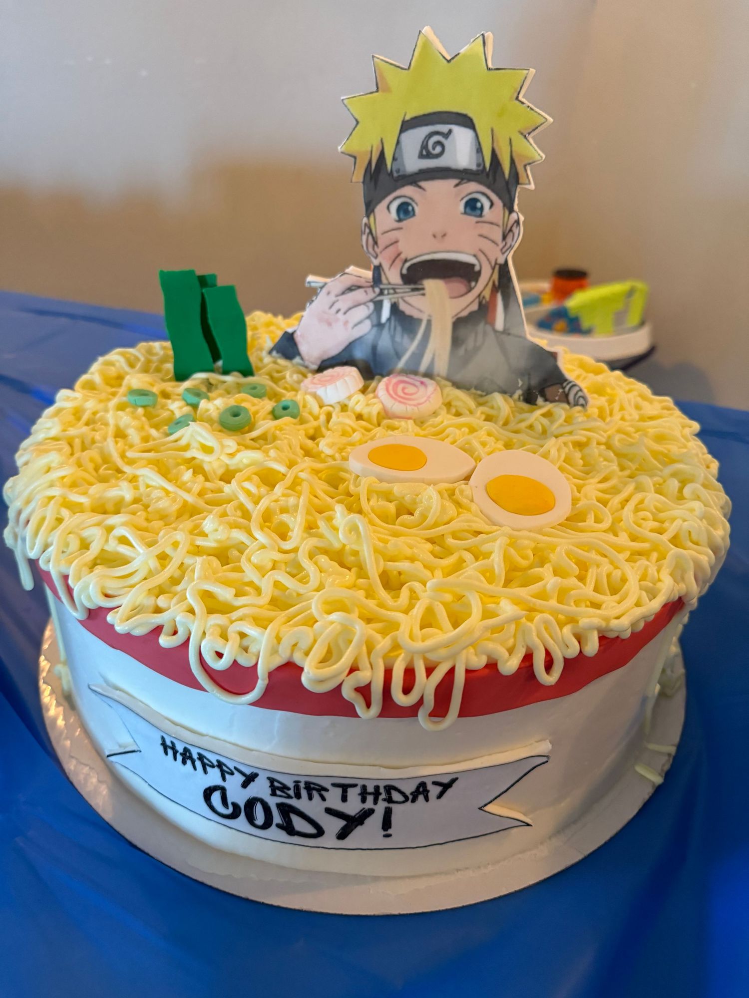 A ramen-themed birthday cake featuring decorative noodles and eggs with an anime character design.