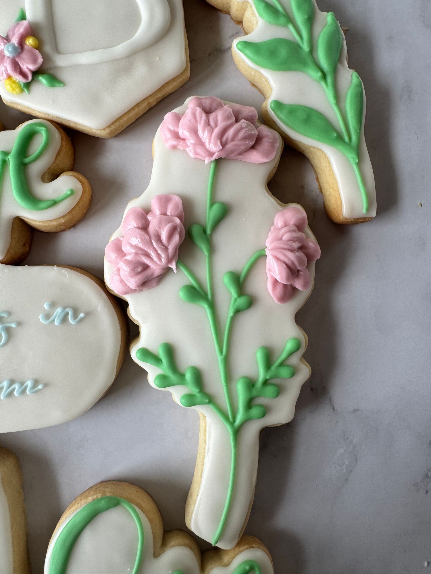 Decorated sugar cookie with delicate pink floral design and green leaves on white royal icing background.