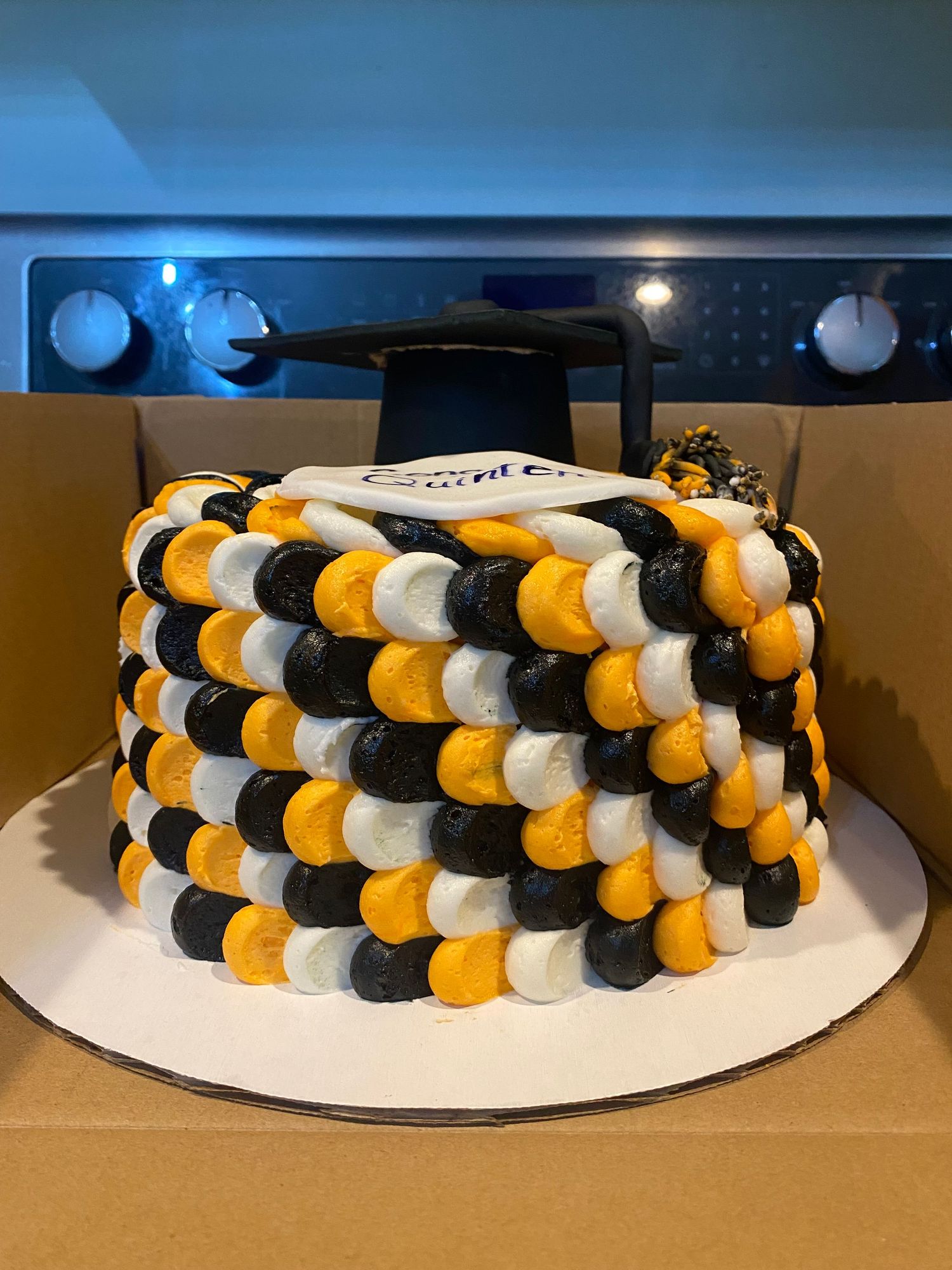 Round cake decorated with alternating black, orange, and white frosting dots in a geometric pattern.