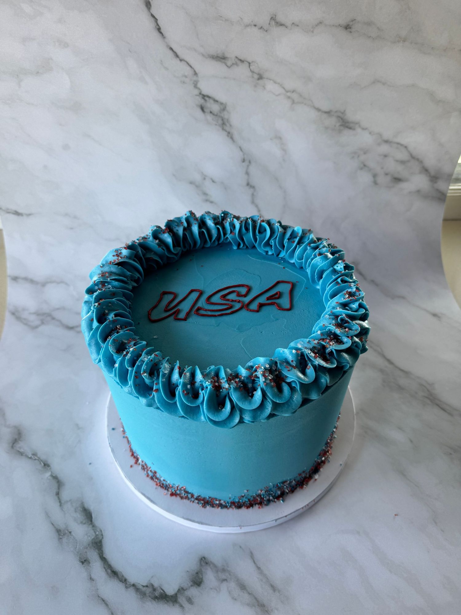 Round blue frosted cake with decorative piping around the edges and text on top.