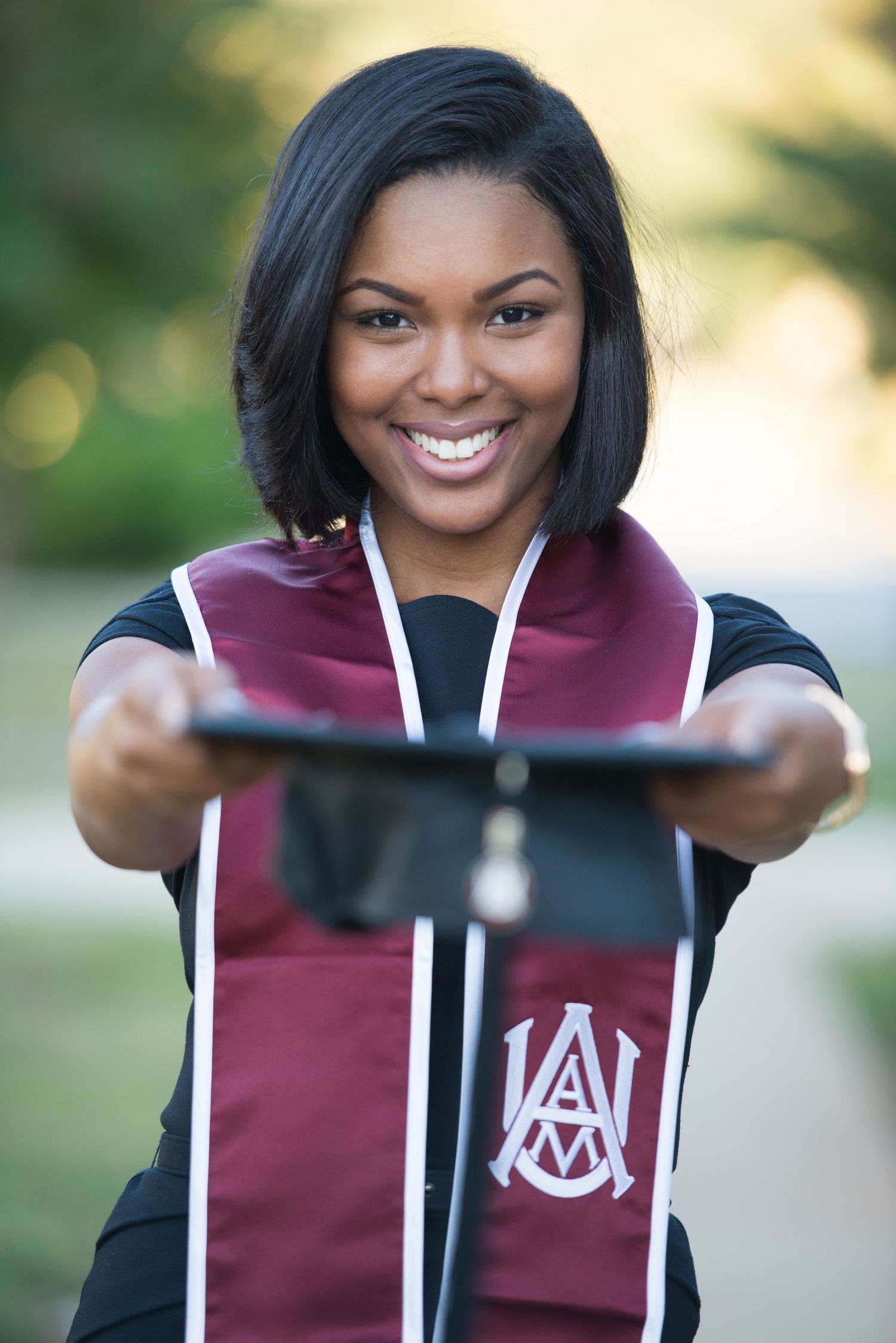Graduate holding up graduation stole with university logo in outdoor setting.