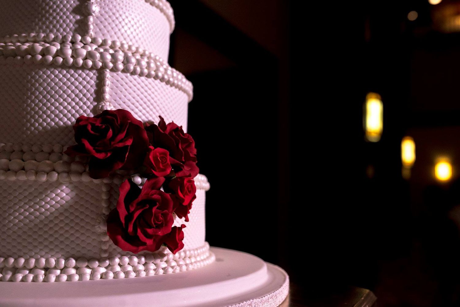 Elegant white wedding cake with red rose decorations on display.