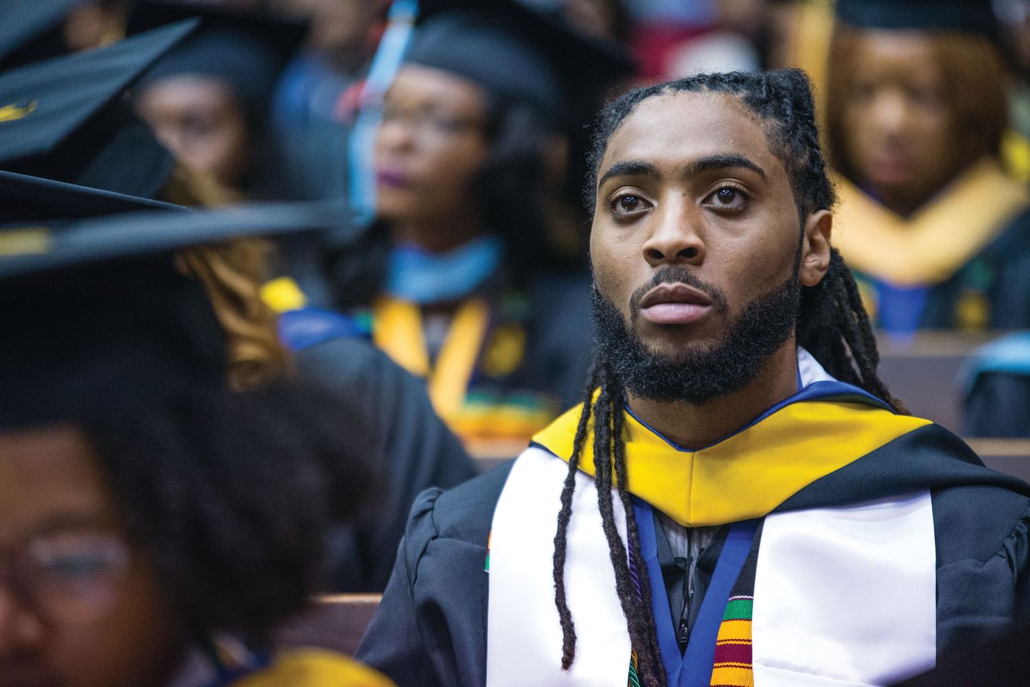 Graduates wearing traditional black caps and gowns with colorful stoles at ceremony.