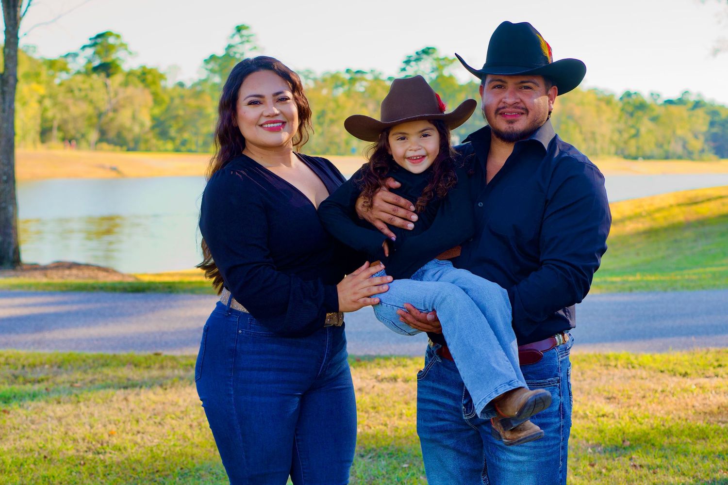 Family maternity photo session outdoors by lake with casual western attire.