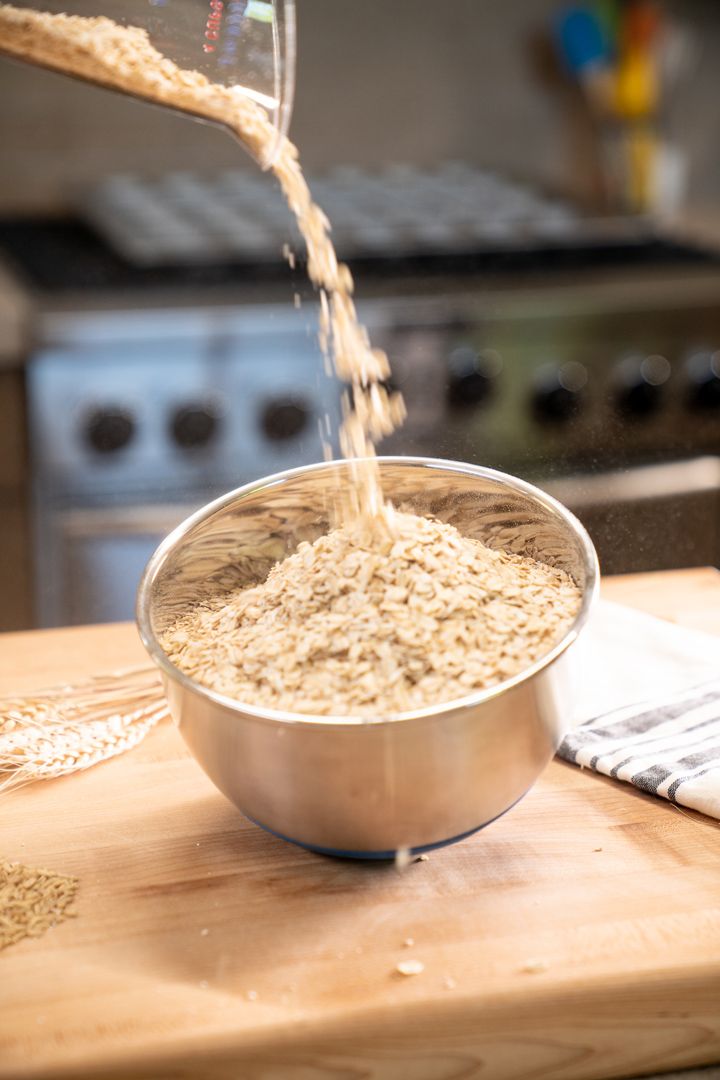 Oats being poured into metal mixing bowls on a wooden surface.