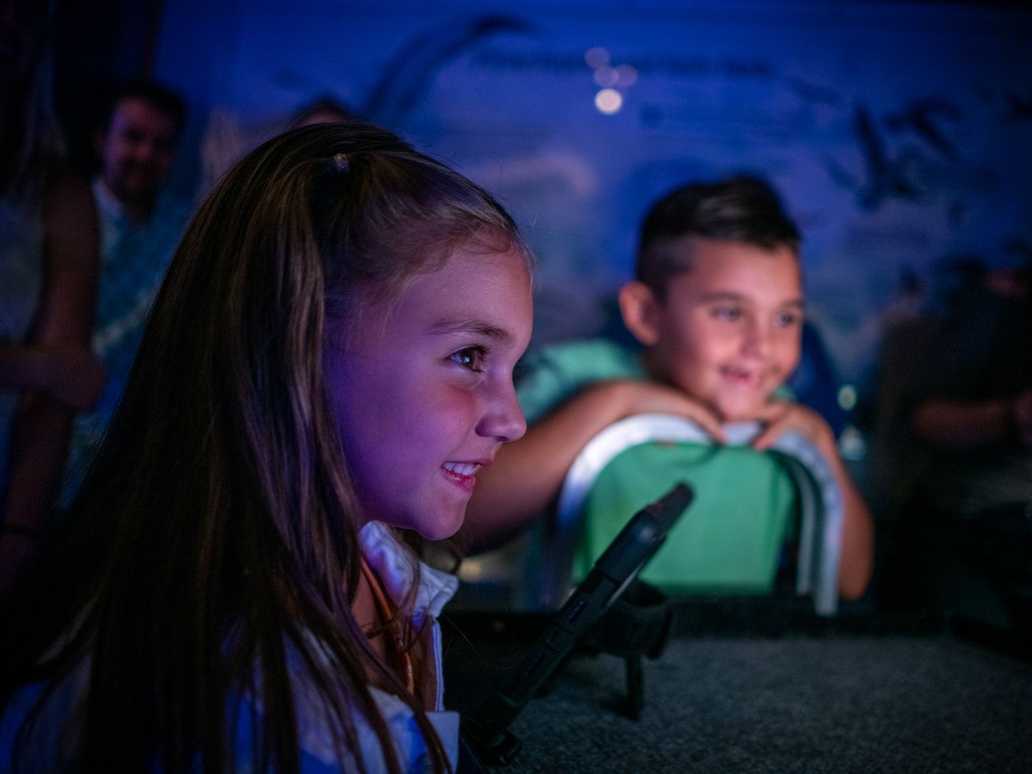 Children sitting in a dark room illuminated by blue lighting.