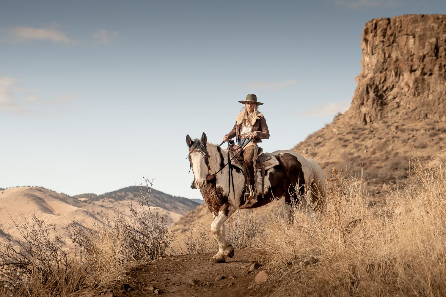 Rider on horseback against rugged desert landscape with mountain backdrop.