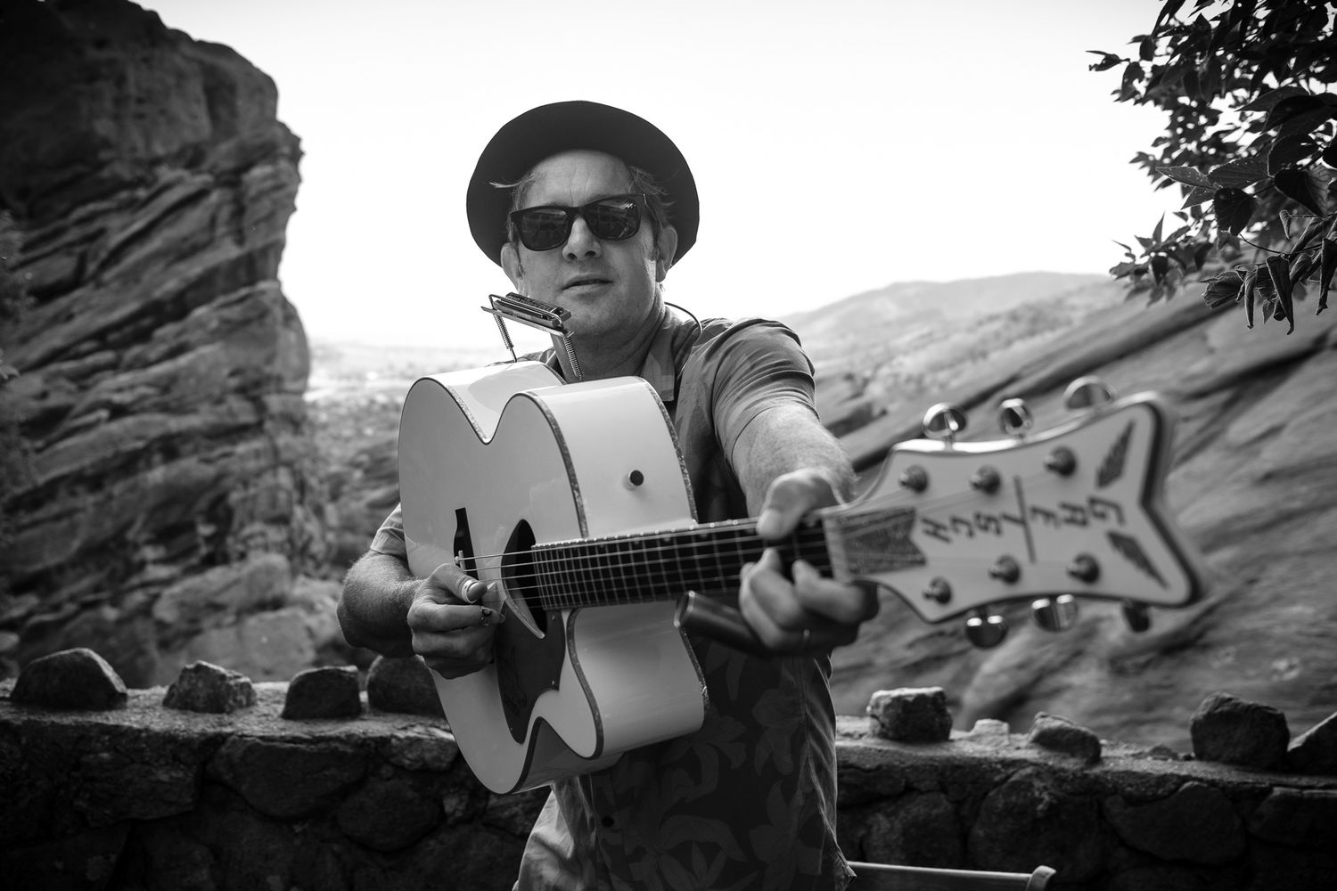 Musician playing acoustic guitar outdoors near rocky cliffs in black and white photography.
