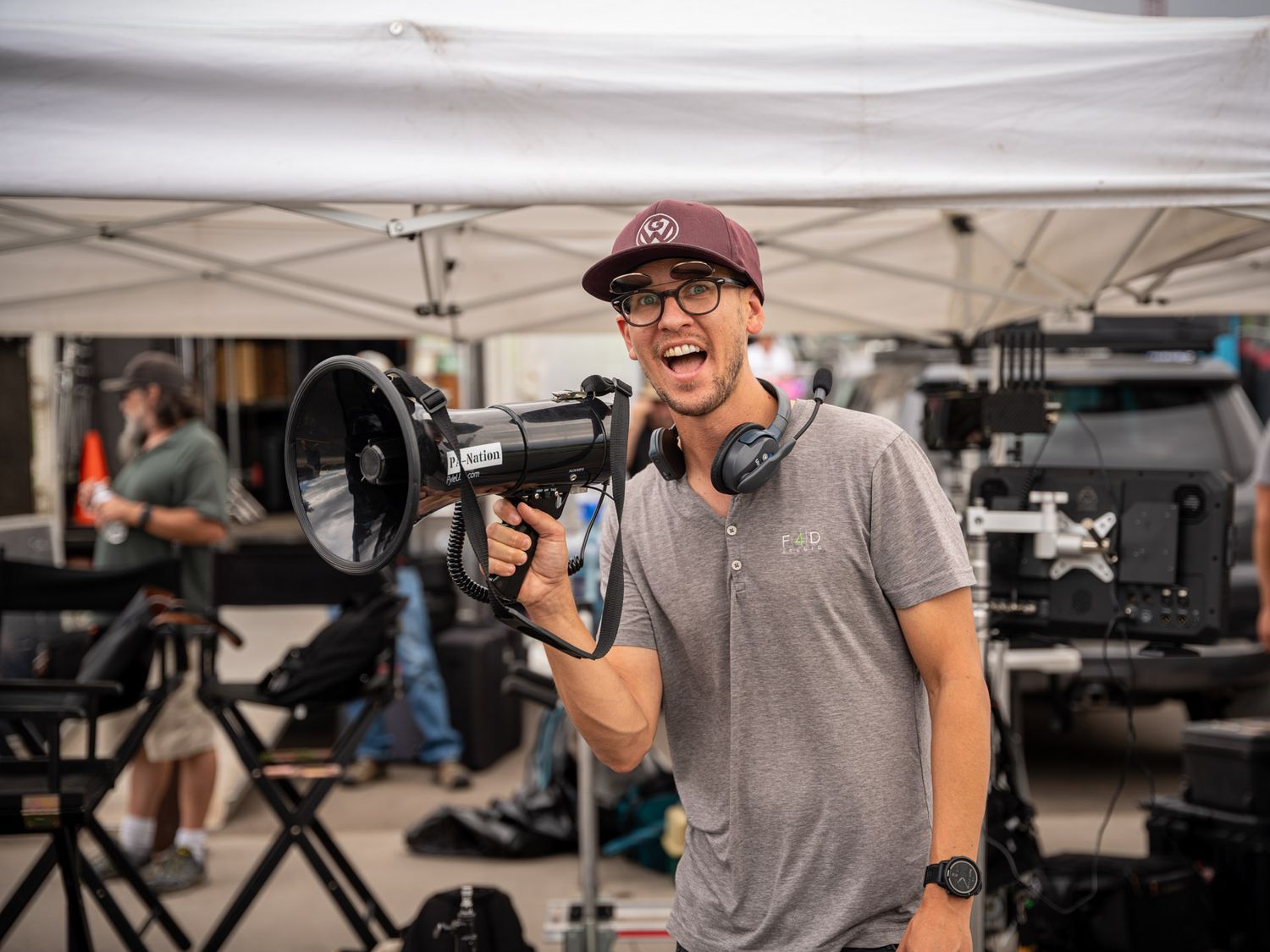 Film production crew with camera equipment working under white tents outdoors.