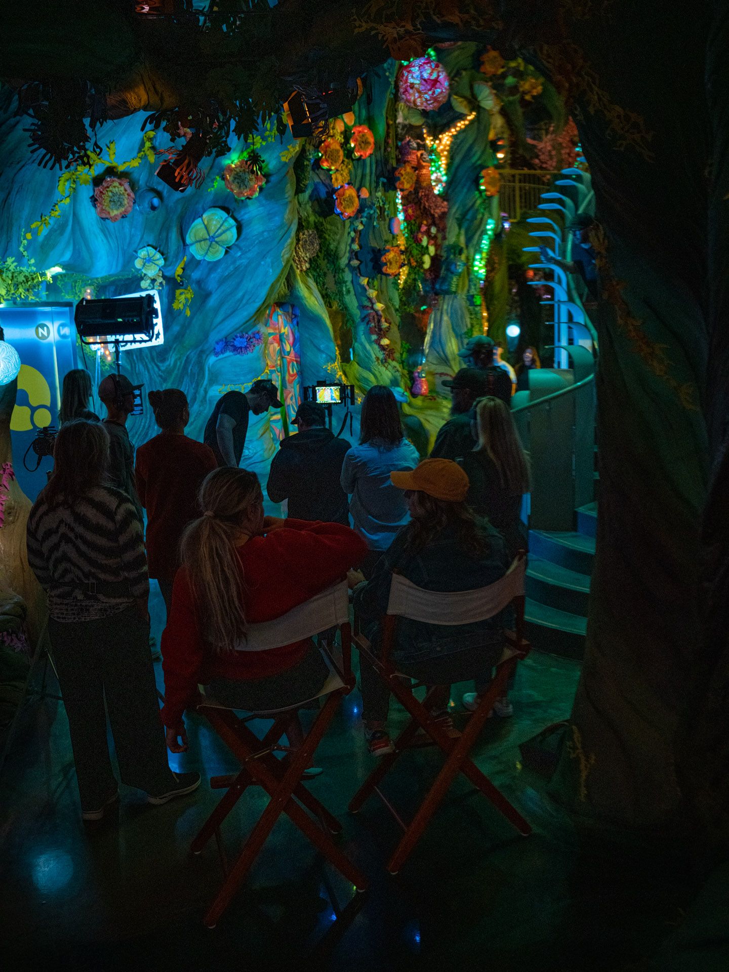 Crowd silhouettes gathered in a dark venue with vibrant blue and green lighting effects.