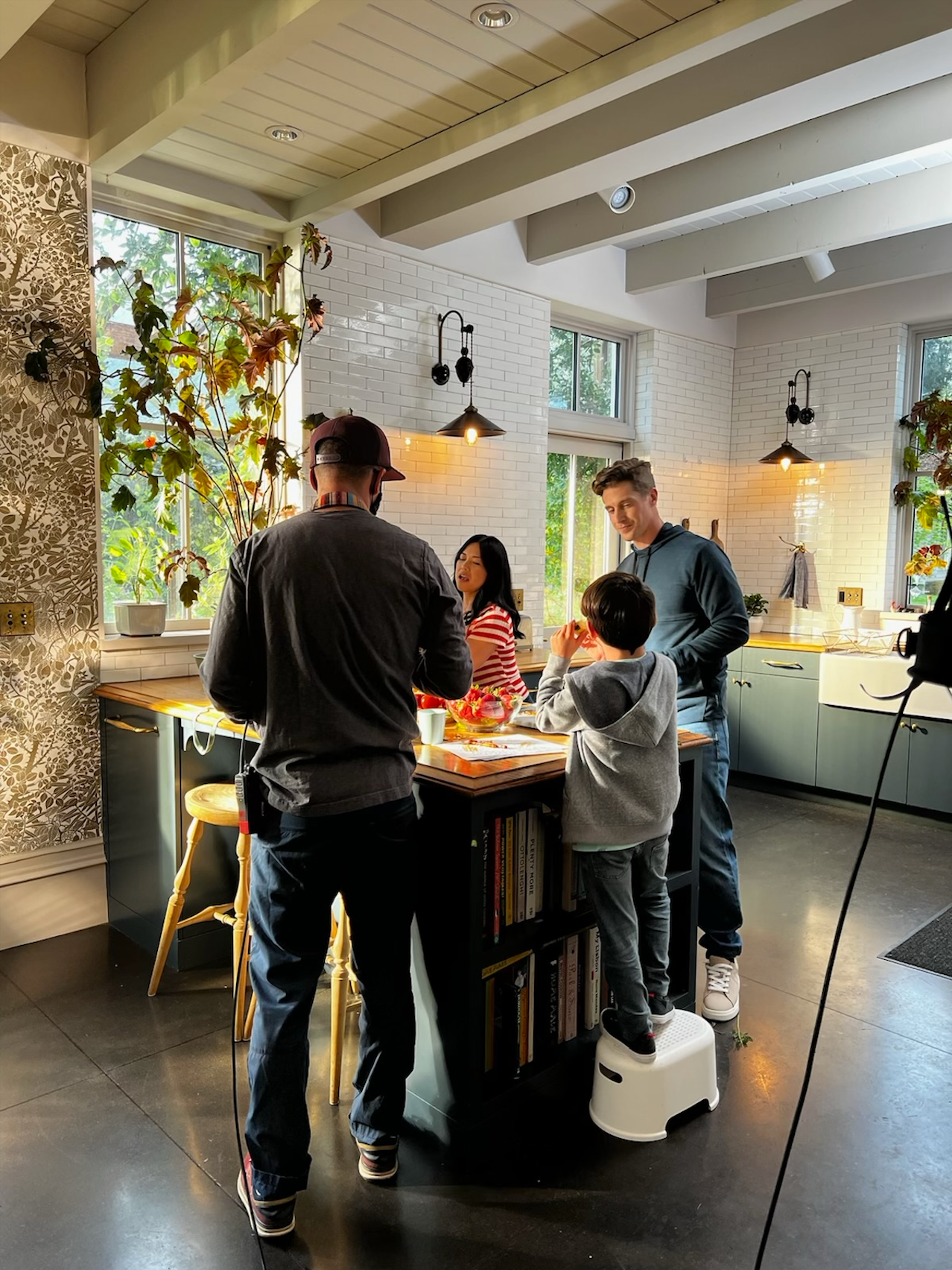 People gathering around a modern kitchen island with exposed wooden beams and pendant lighting overhead.