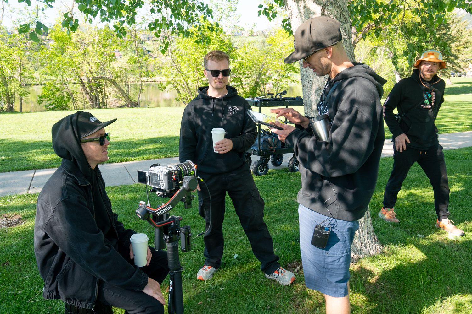 A group sits together on grass having a picnic gathering in a sunny park setting.