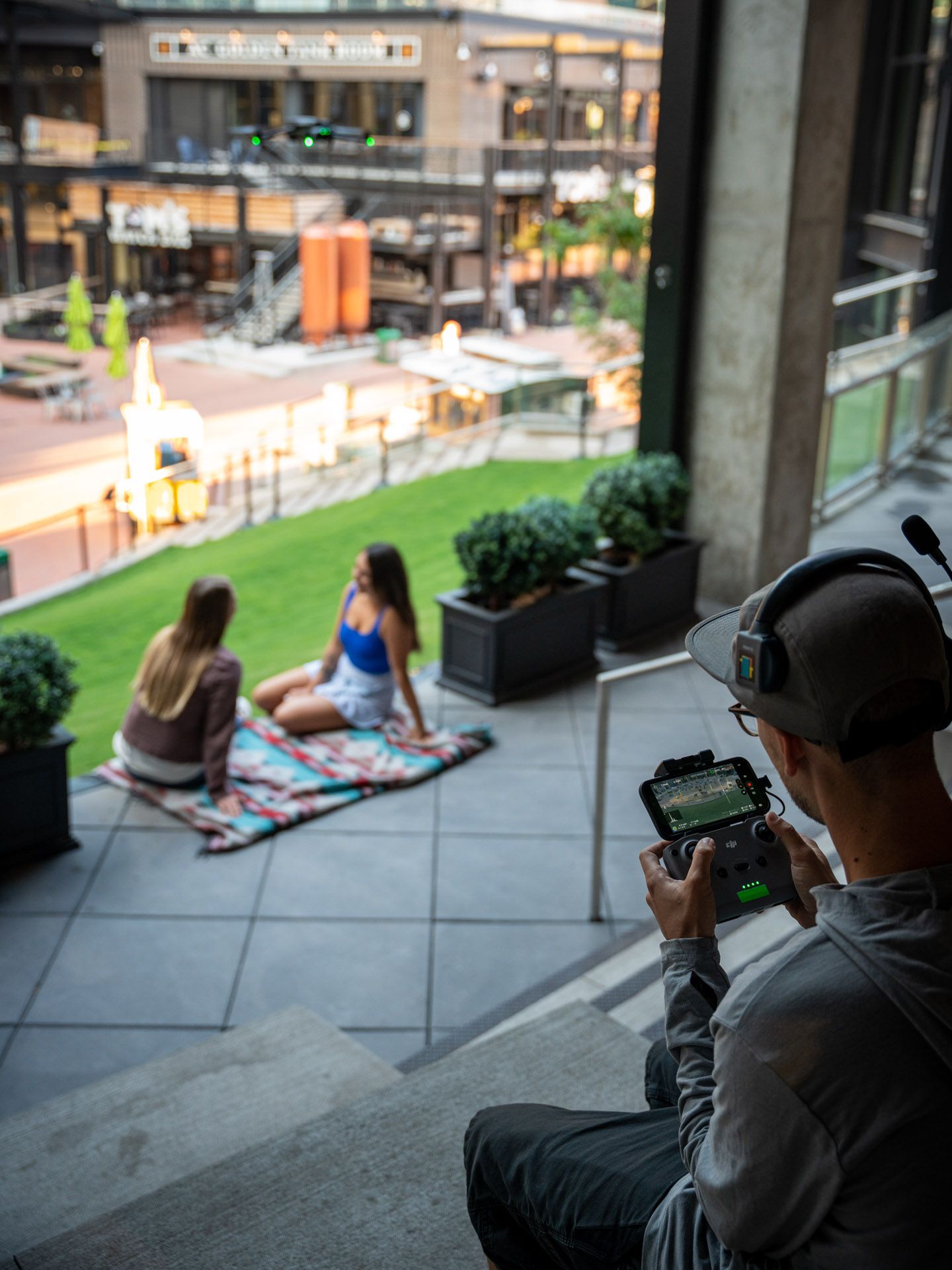 Three people relaxing on an urban patio while one films with a handheld camera.