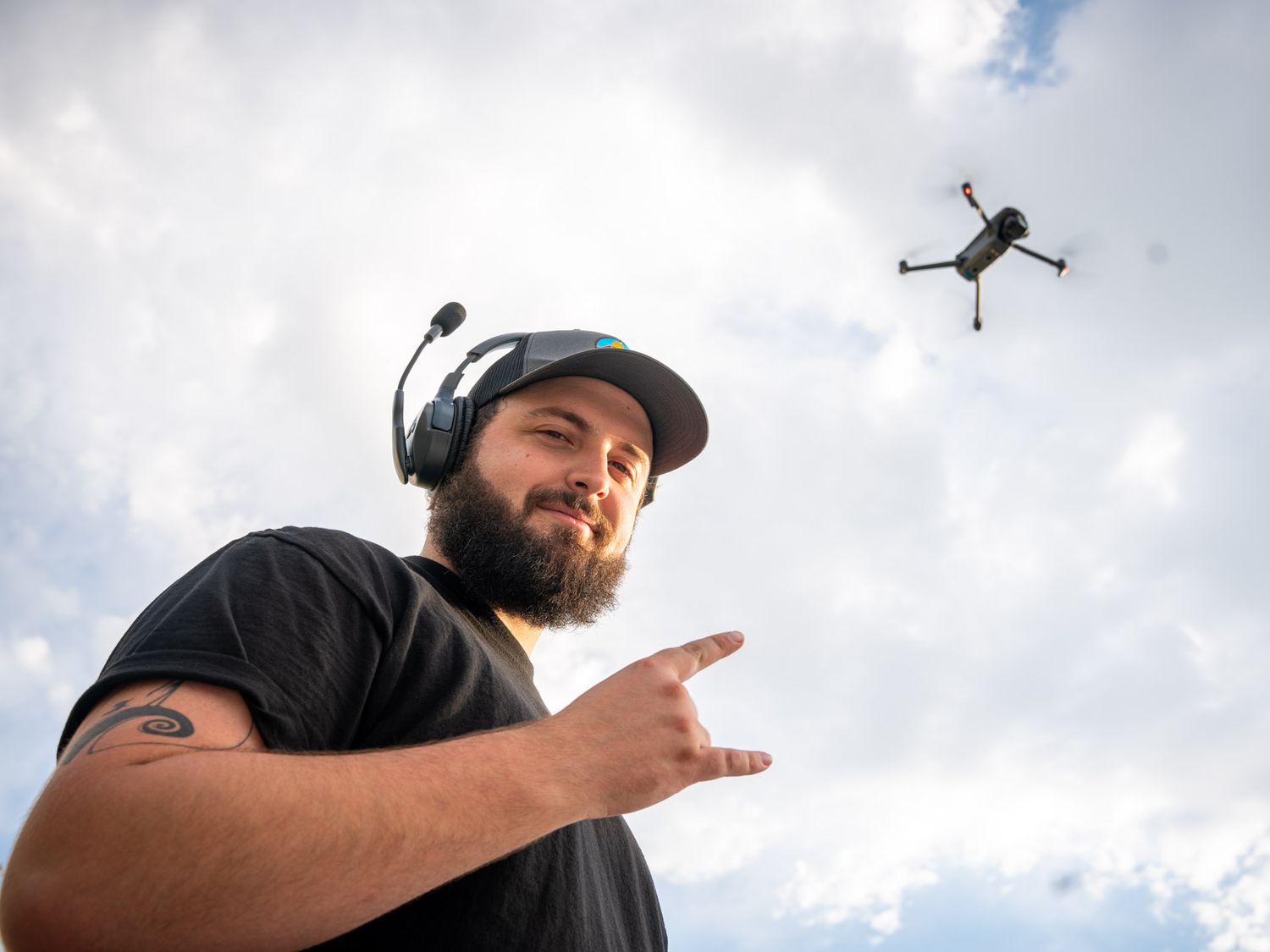 Camera operators and drone flying against a cloudy sky in an outdoor filming shoot.