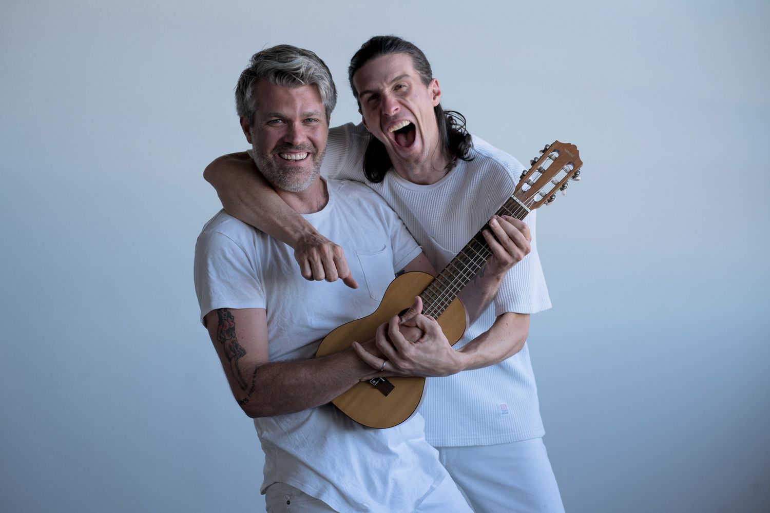 Two people in white shirts sharing a moment with a guitar.