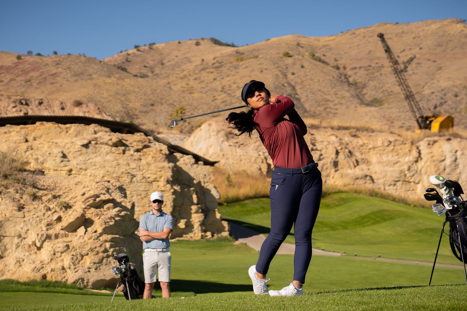 Golfer practicing putting on desert course with rocky hills in background.
