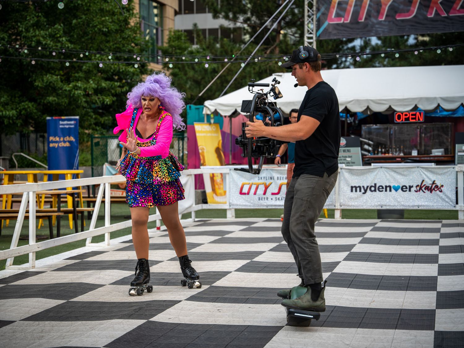 Colorfully dressed performers being filmed on a checkered outdoor stage setup.