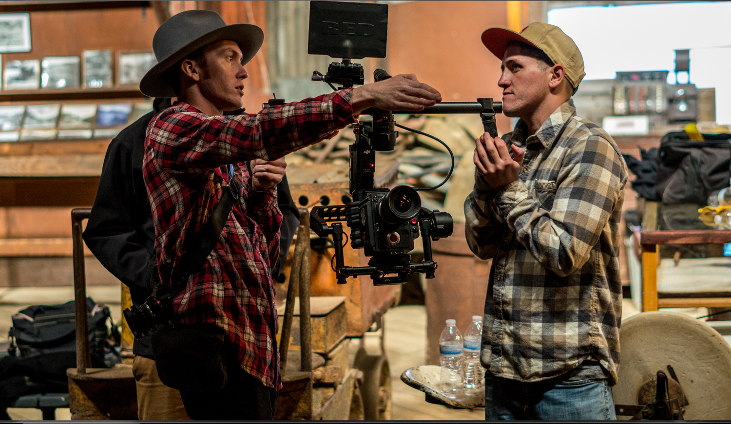 Two people in plaid shirts interact with firearms at what appears to be a retail counter or workshop space.