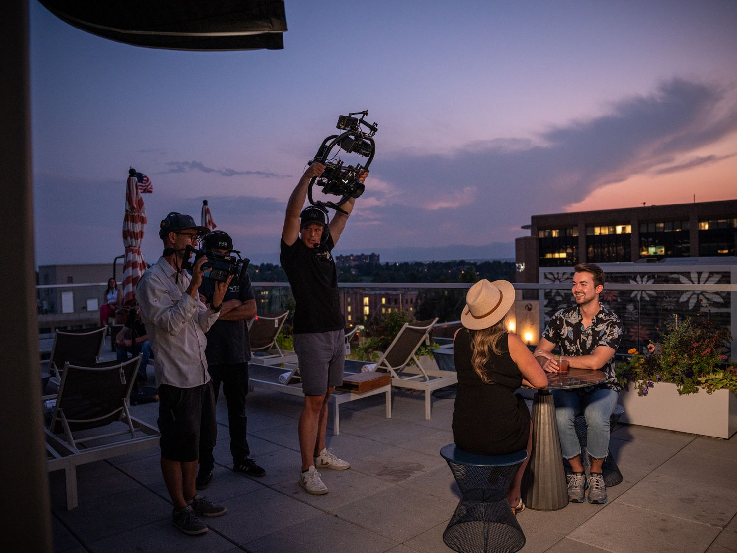 Film crew working during sunset on a rooftop with camera equipment and lighting gear.