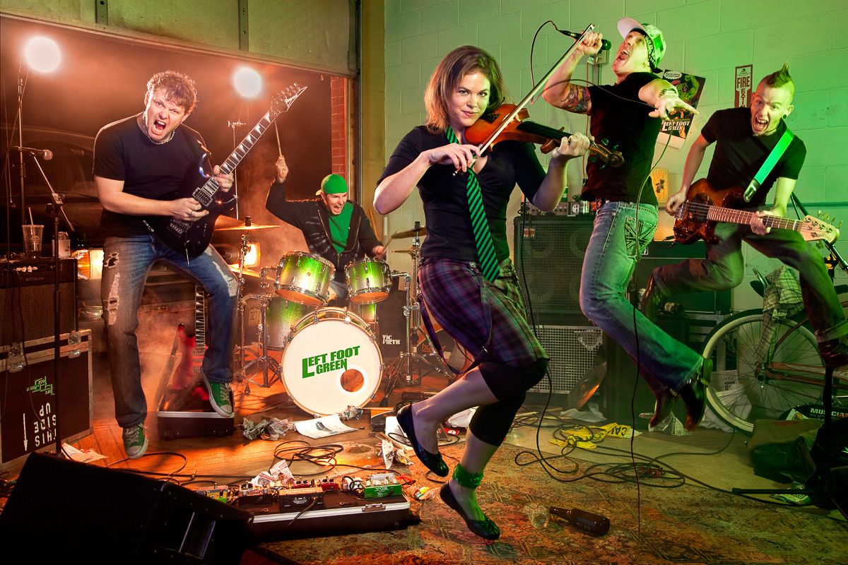 Energetic rock band performs on stage with violin player in spotlight and green lighting effects.