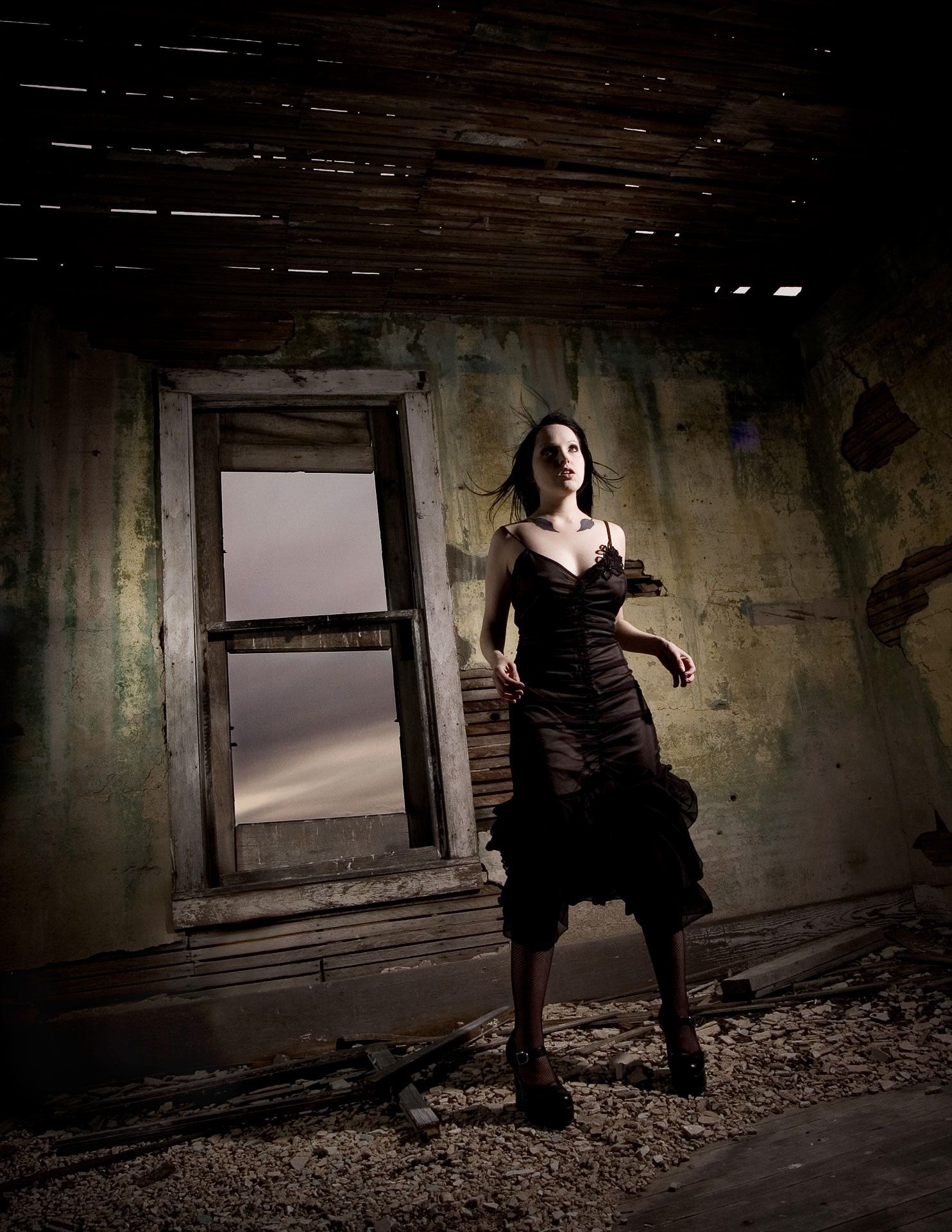 Dramatic portrait in dark dress standing in abandoned room with window.