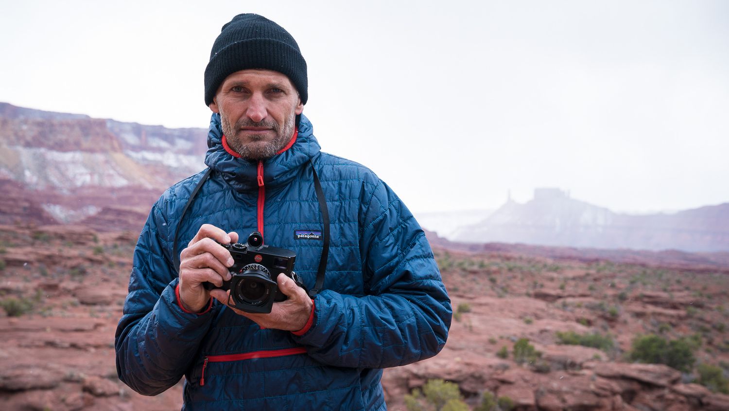 Photographer in winter gear capturing shots in snowy red rock desert landscape.