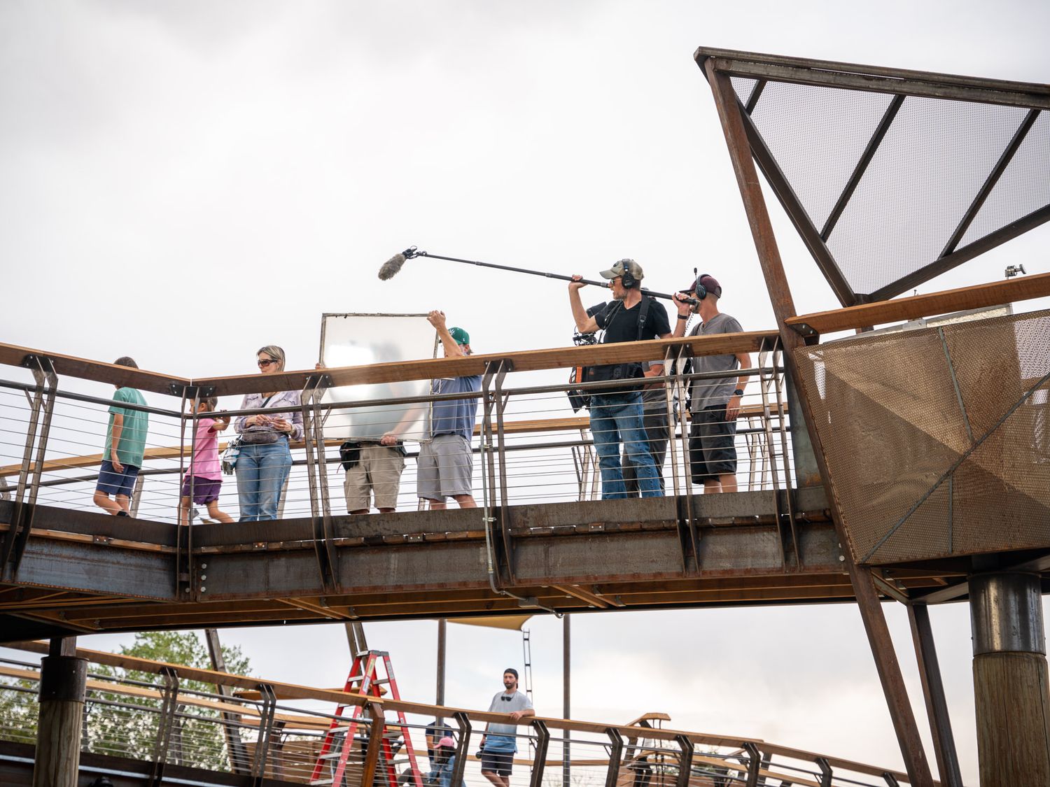 Group of people walking across elevated wooden walkway structure outdoors.