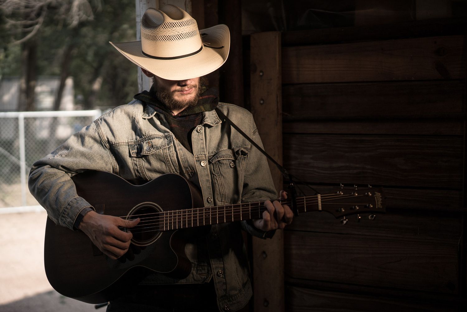 Cowboy musician performs with acoustic guitar on wooden porch in vintage setting.