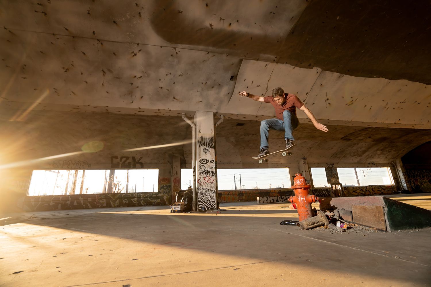 Skateboarder performing trick on ramp in abandoned industrial space with dramatic lighting.
