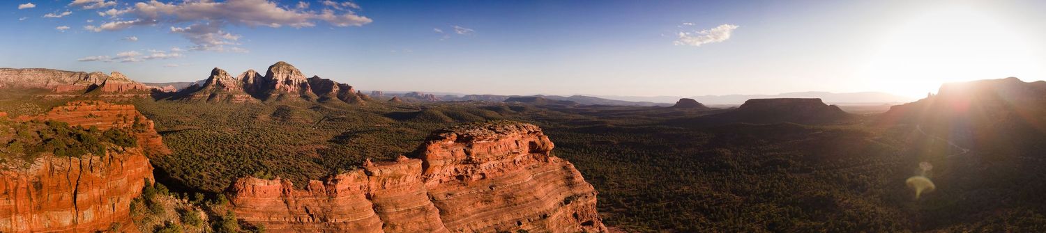 Panoramic sunset view of red rock formations and mountains in Sedona Arizona with dramatic clouds and shadows.