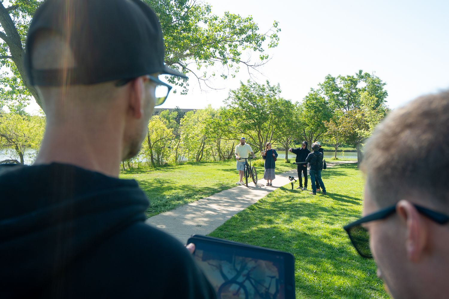 People gather on a sunny grassy lawn while others observe from behind in a park-like setting.