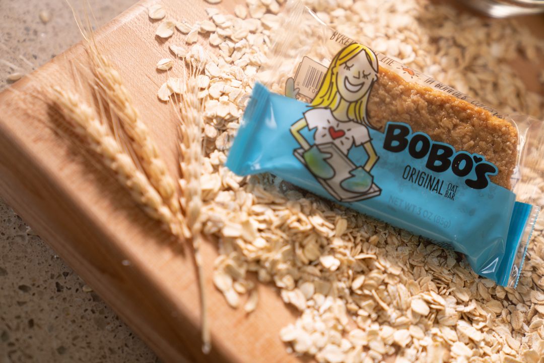 Scattered oats and blue protein bar packaging on a wooden surface.