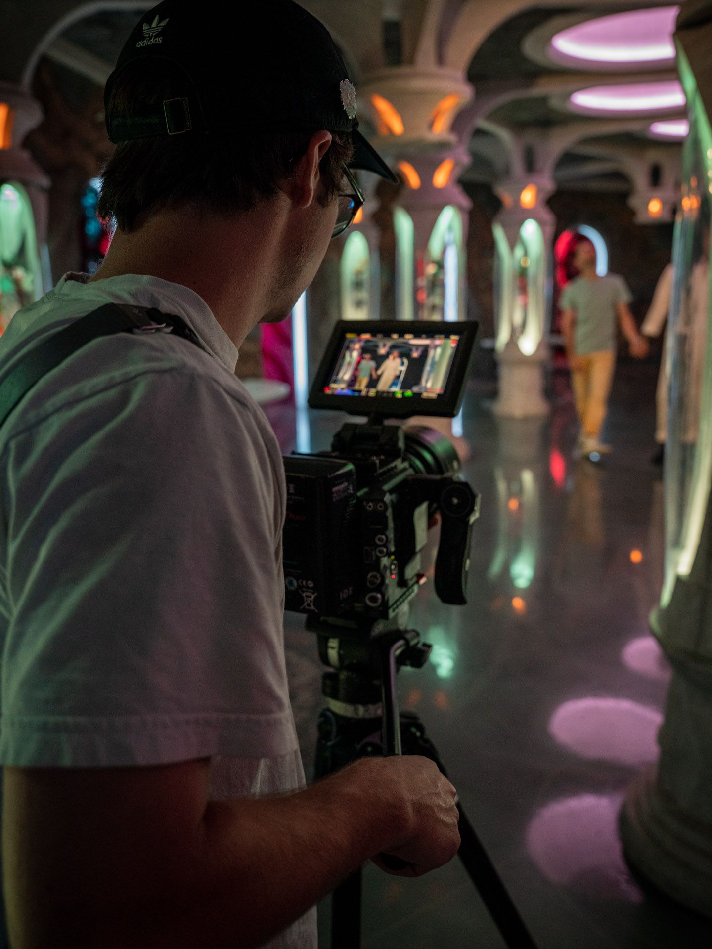 Film crew working in a dimly lit space with colorful ambient lighting.