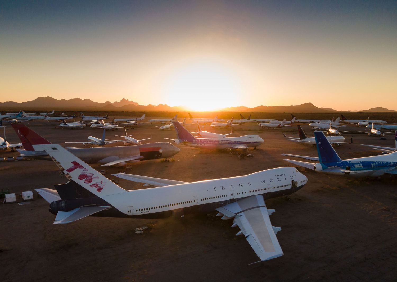Parked airplanes at small desert airport during sunrise with golden light streaming across the tarmac.