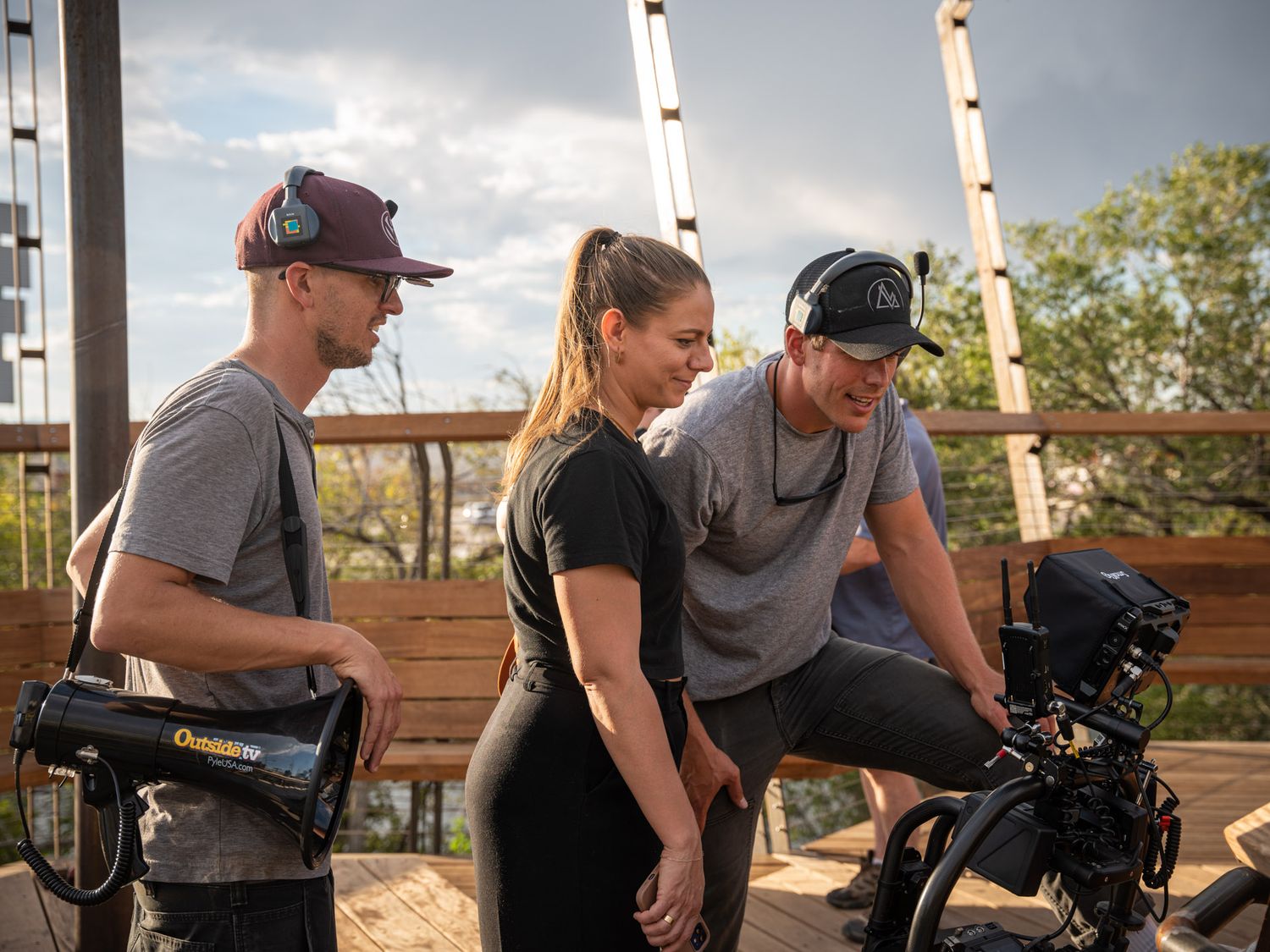 Camera operators filming on location with equipment on outdoor deck.