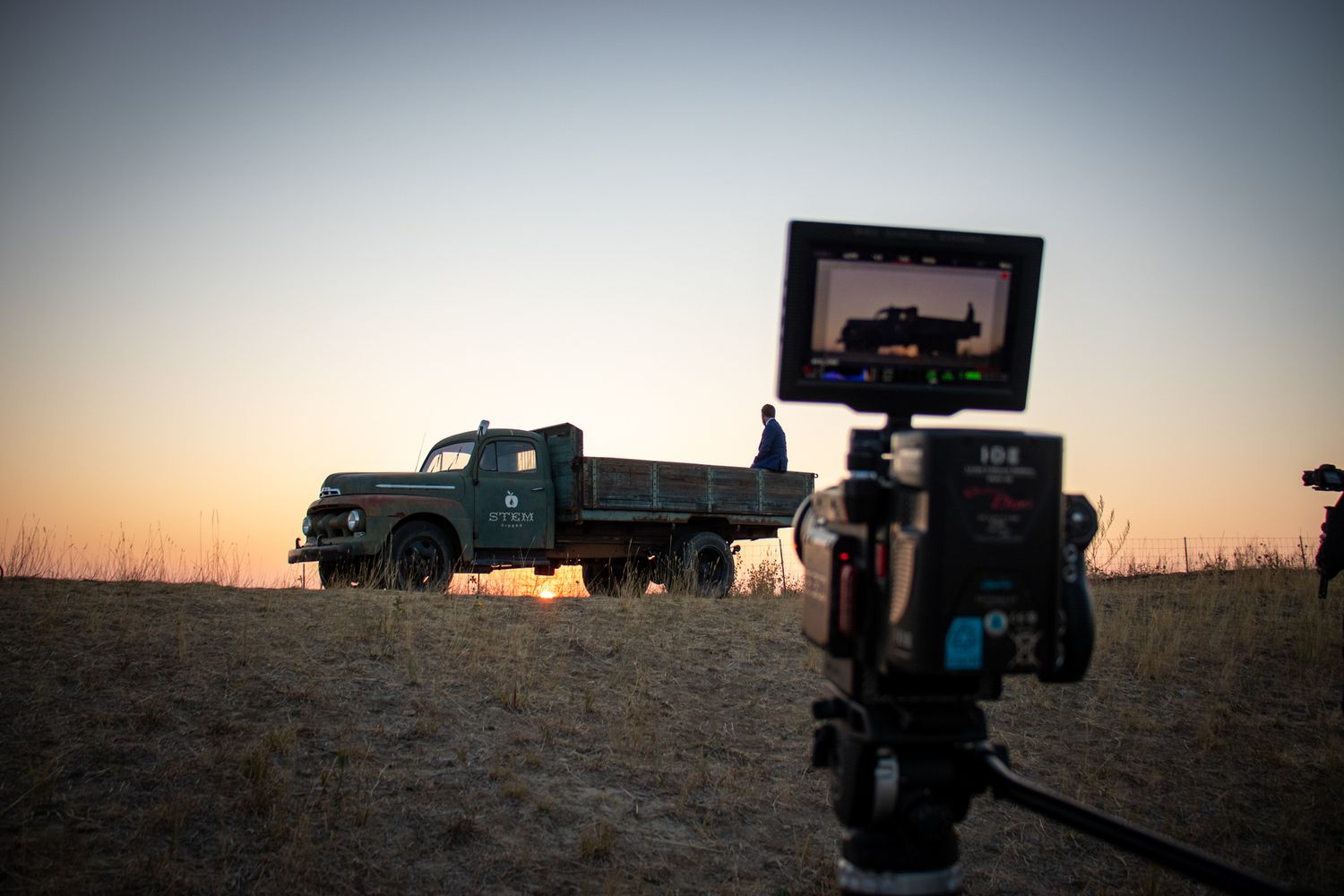 Military vehicles parked in a desert landscape at sunset with silhouettes against an orange sky.