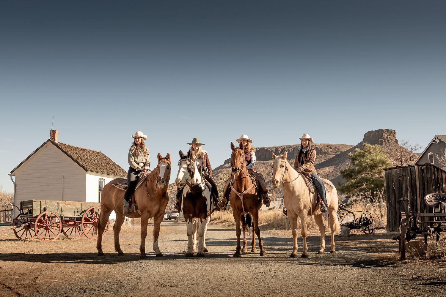 Group of riders on horseback lined up against desert landscape with buildings.