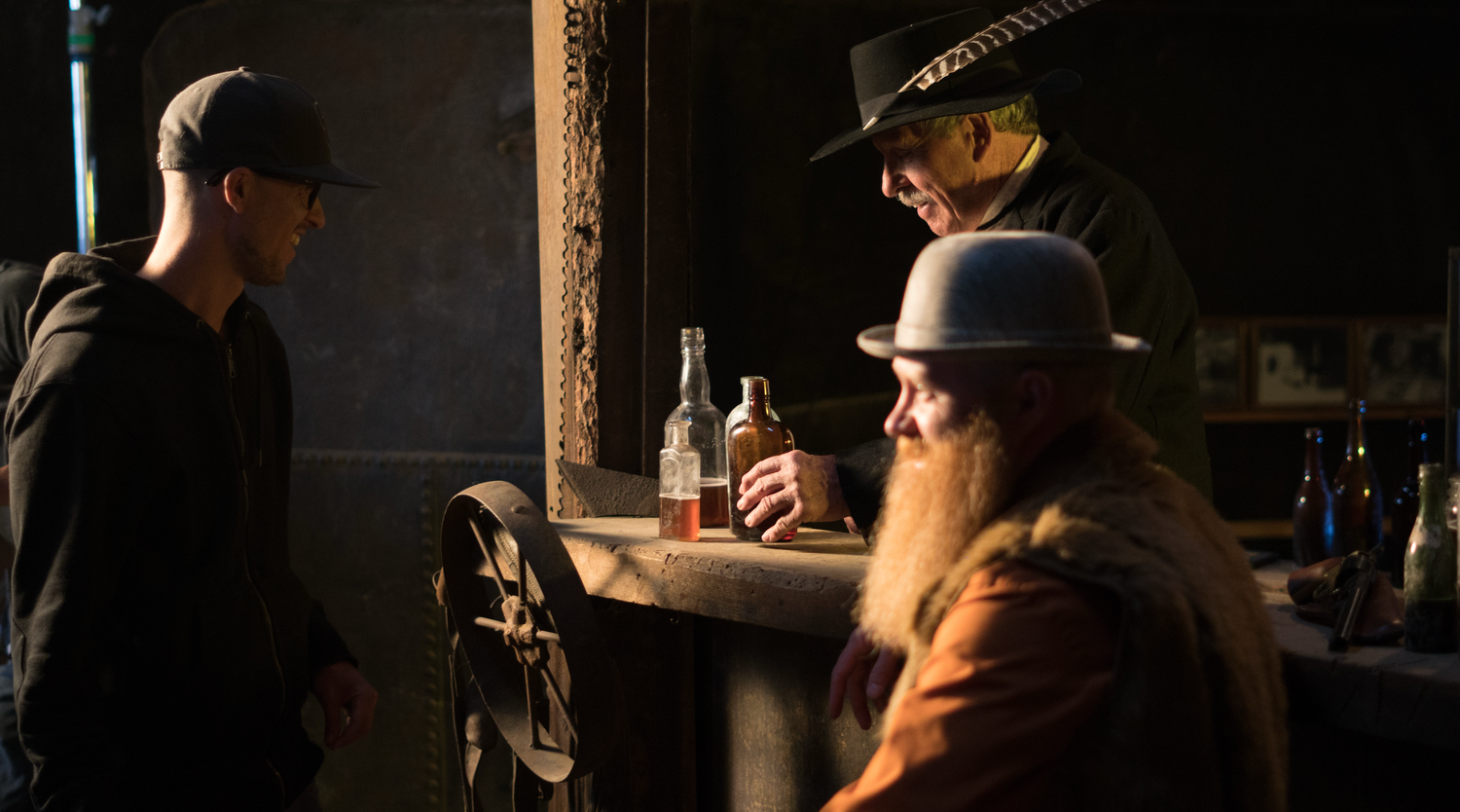 Bartender in hat pouring drinks at dimly lit bar counter during evening service.