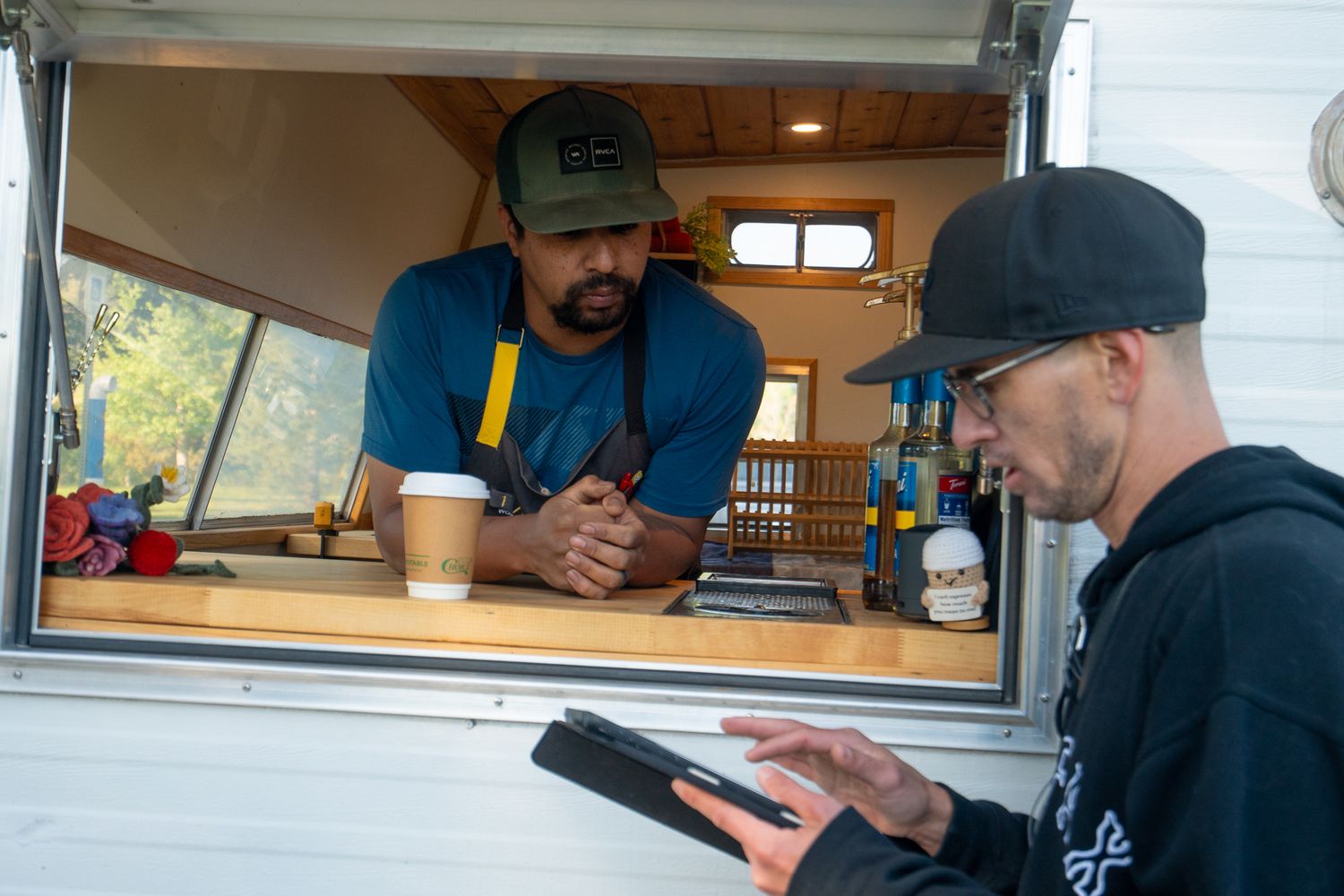 People ordering food from a food truck window while others wait in line outside.