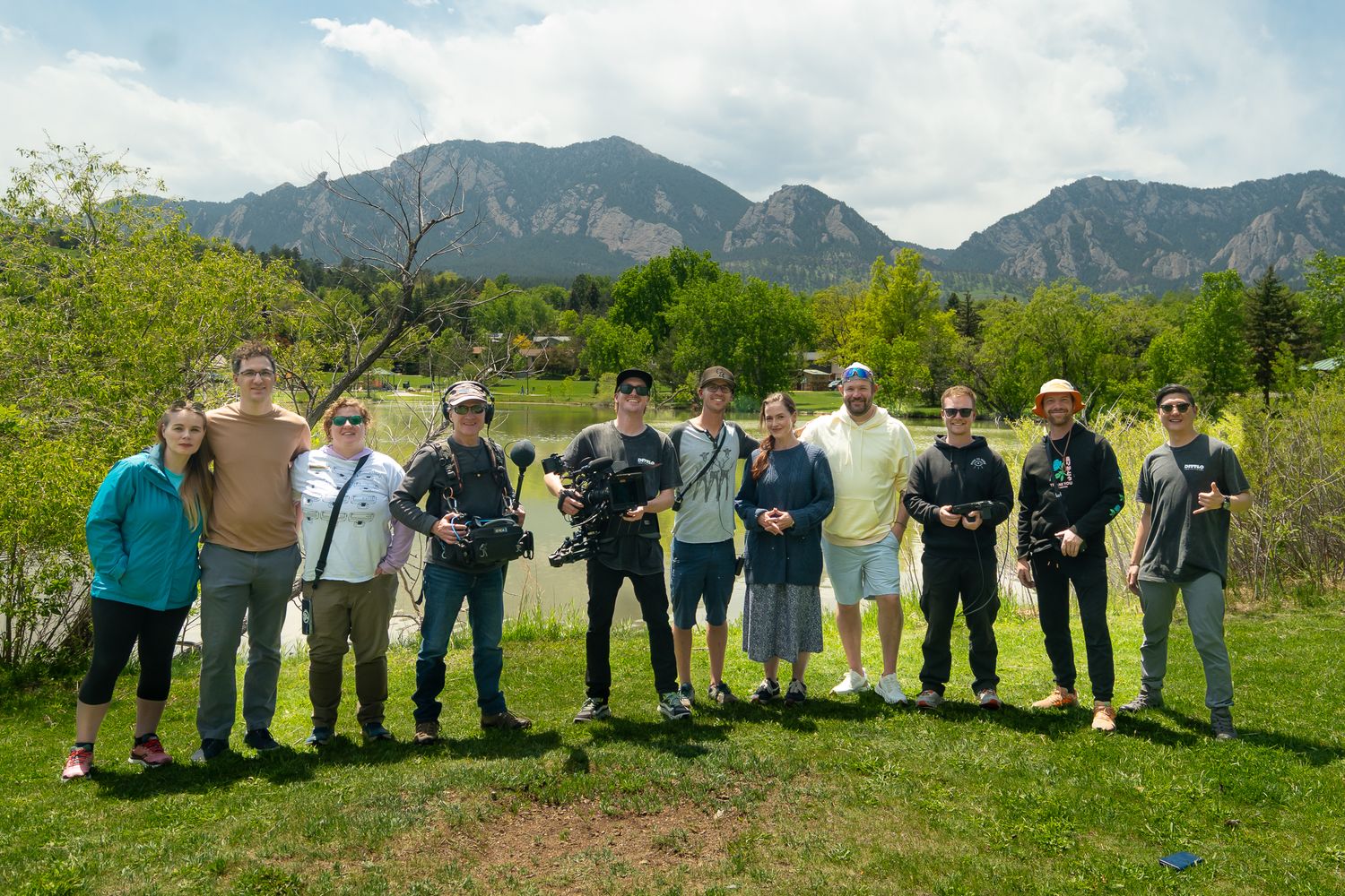 A group of people lined up outdoors against a scenic mountain backdrop with blue skies and green grass.