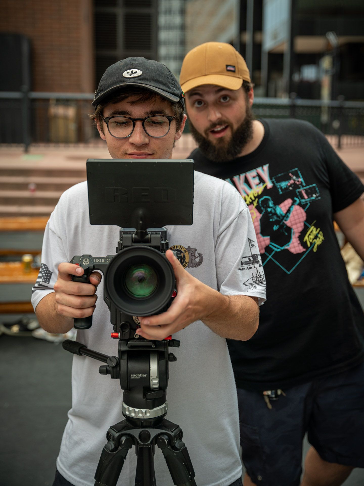 Camera operators setting up professional filming equipment on tripods outdoors.