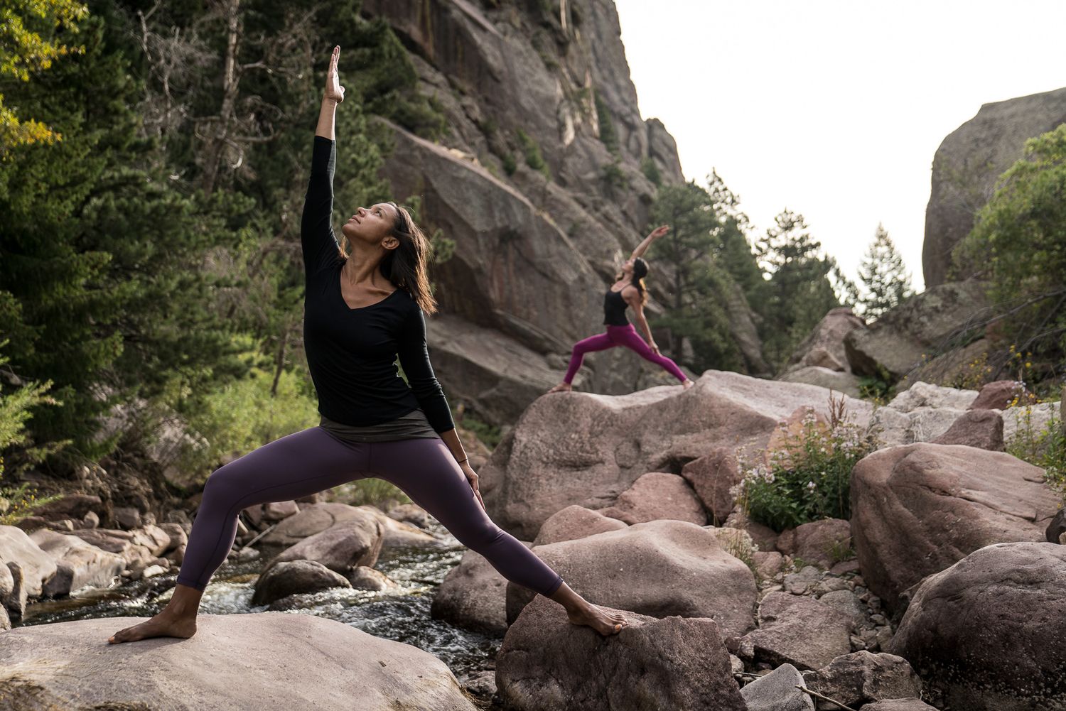 Two people practicing yoga poses on rocky mountain terrain.