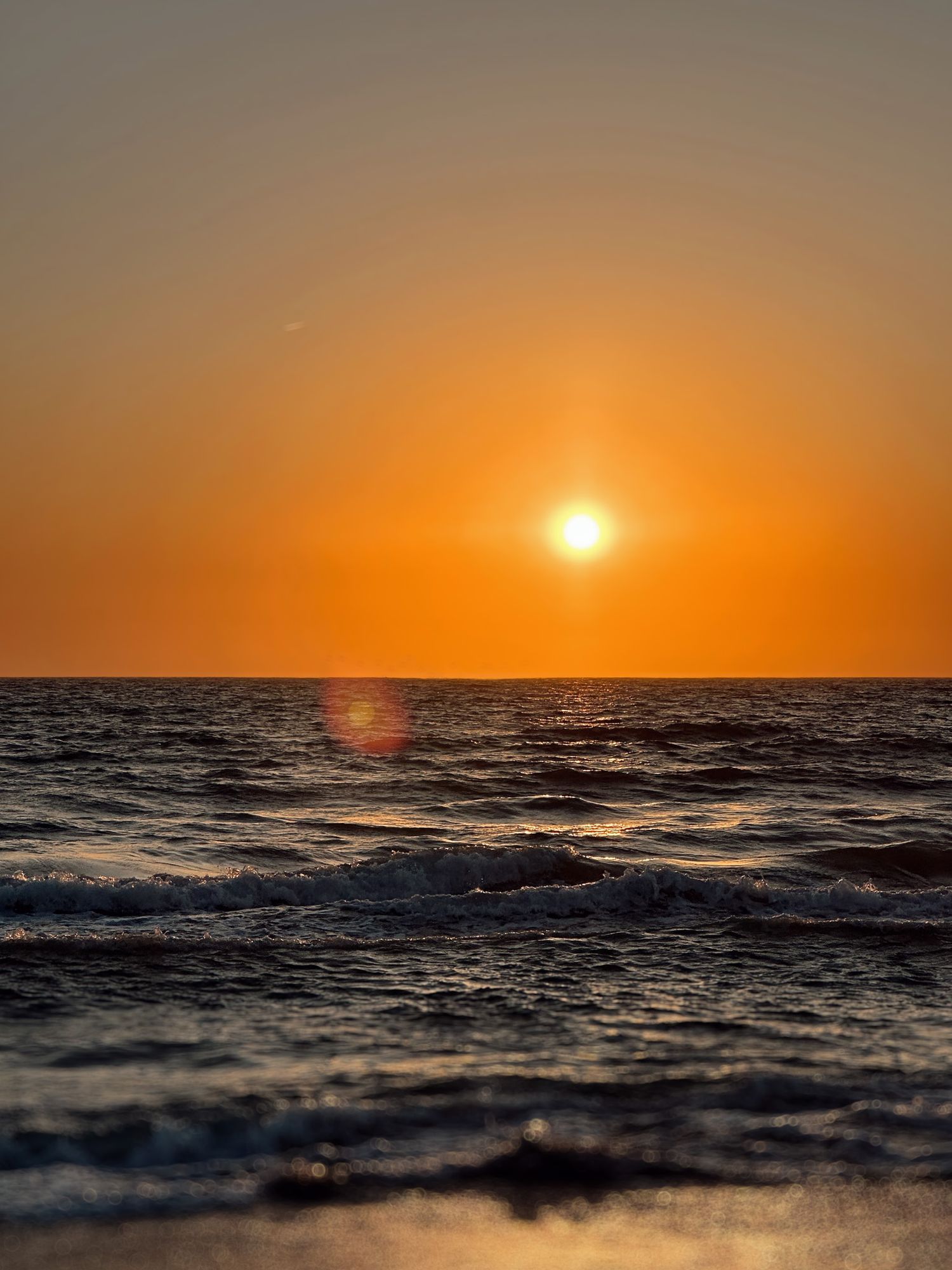 A vibrant orange sunset over dark ocean waves creates a stunning silhouette against the horizon.